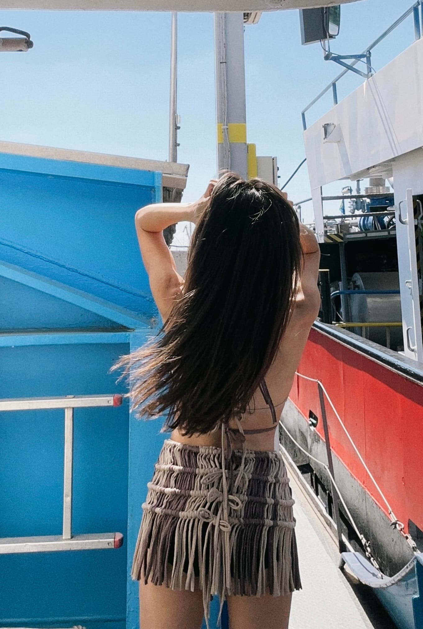Rear view of a woman wearing a backless knit fringe mini dress outdoors on a boat.