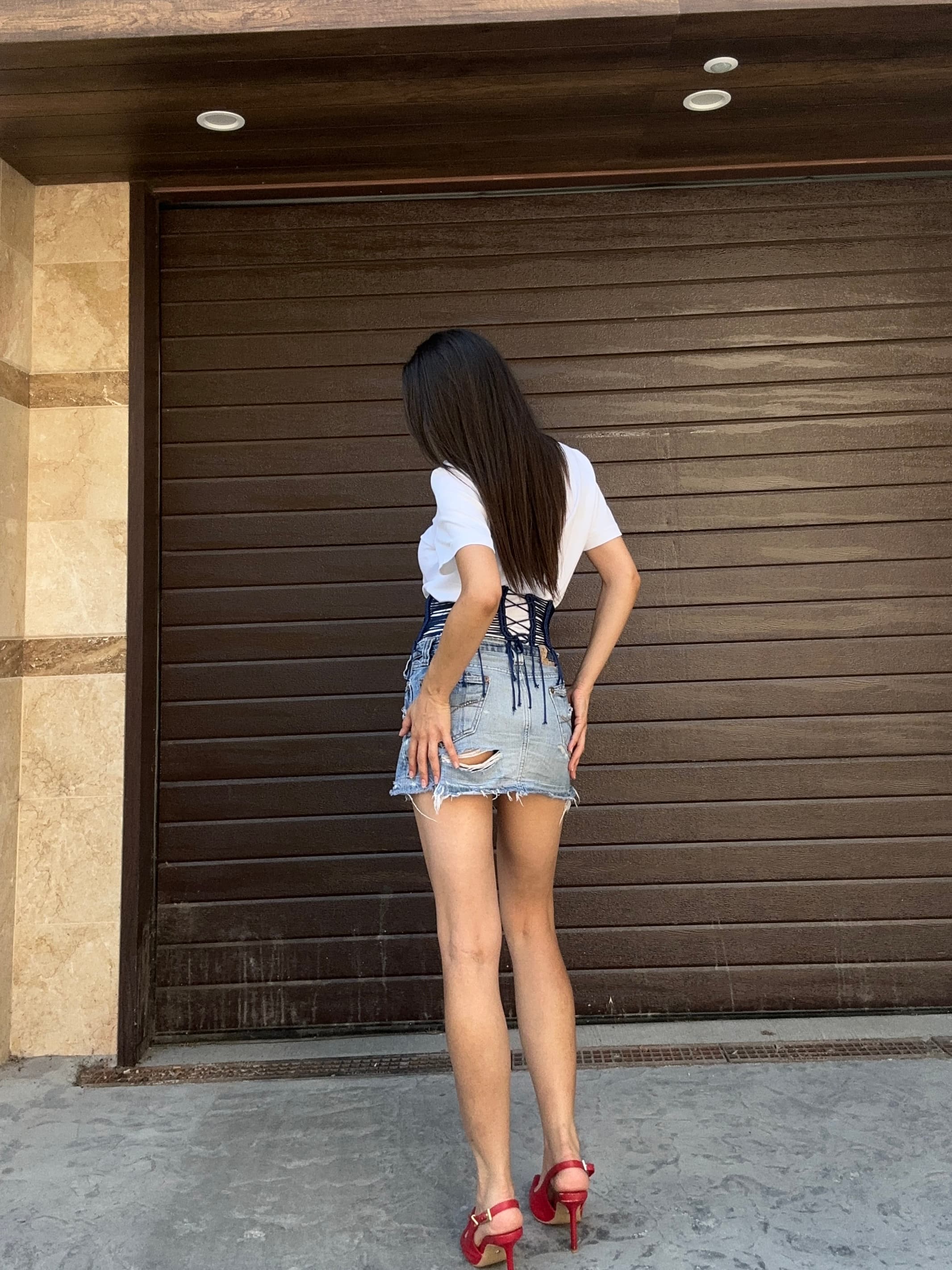 A woman facing away, wearing a wide corset waist belt over a white t-shirt and denim skirt.